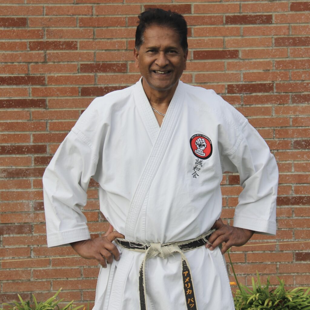 A photograph showing Vassie Naidoo Shihan standing in front of a brick wall.