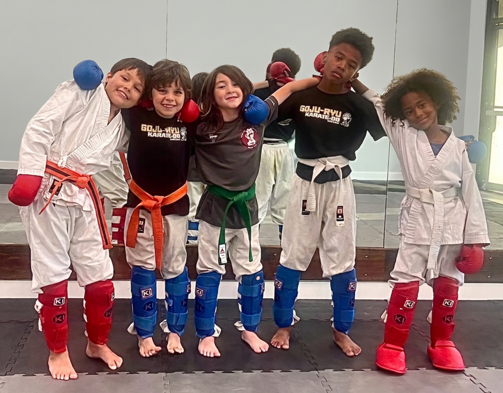 Five young karate students standing side by side in gear with arms around each other