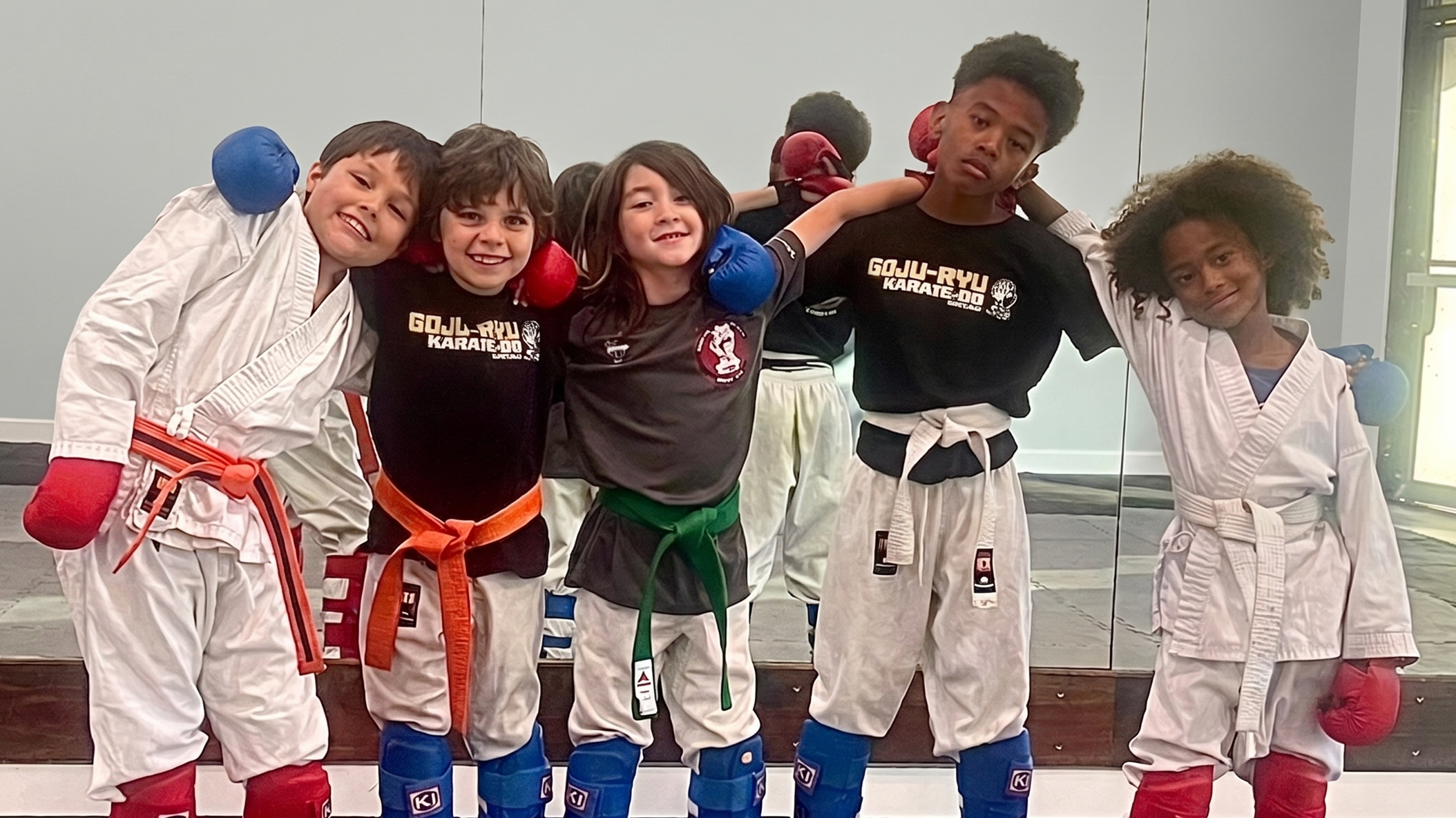 Five smiling young karate students standing side-by-side in sparring gear on the mat at Karate of LA.