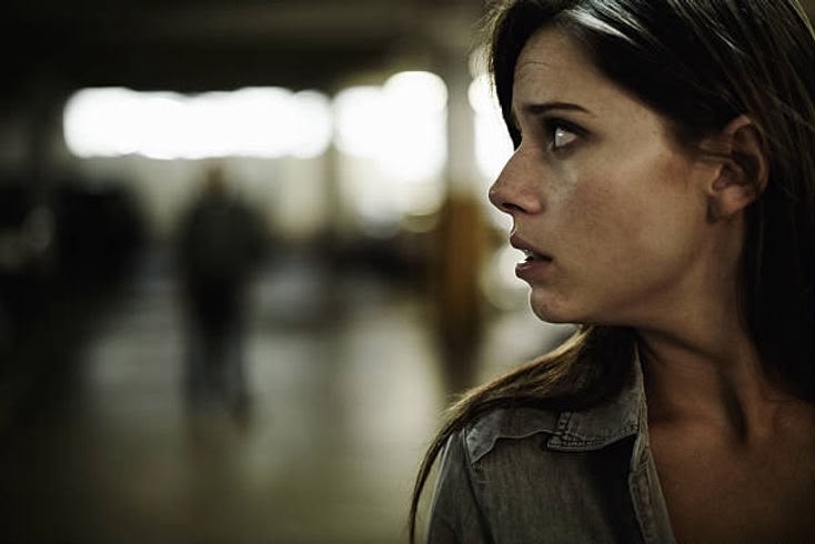 A woman looks back over her shoulder with an alert expression in a dim parking garage, illustrating the self-defense concept of running to safety.