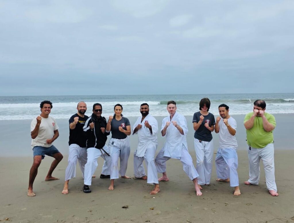 Santa Monica Martial Arts Dojo Community A large group of karate students and martial artists posing together on the sand at Santa Monica Beach after an outdoor session.