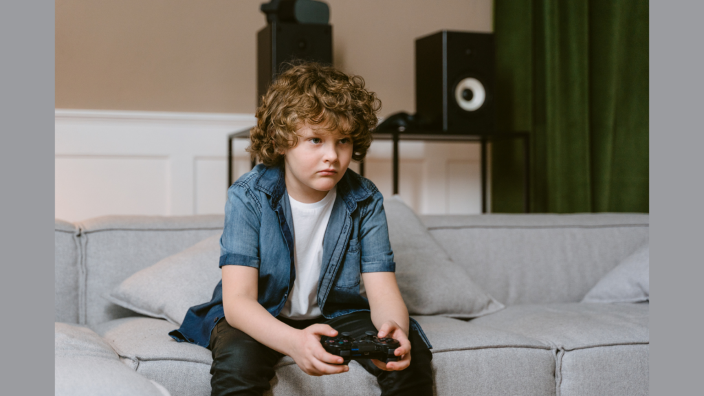 A young boy with curly hair sitting on a couch holding a video game controller looking intense