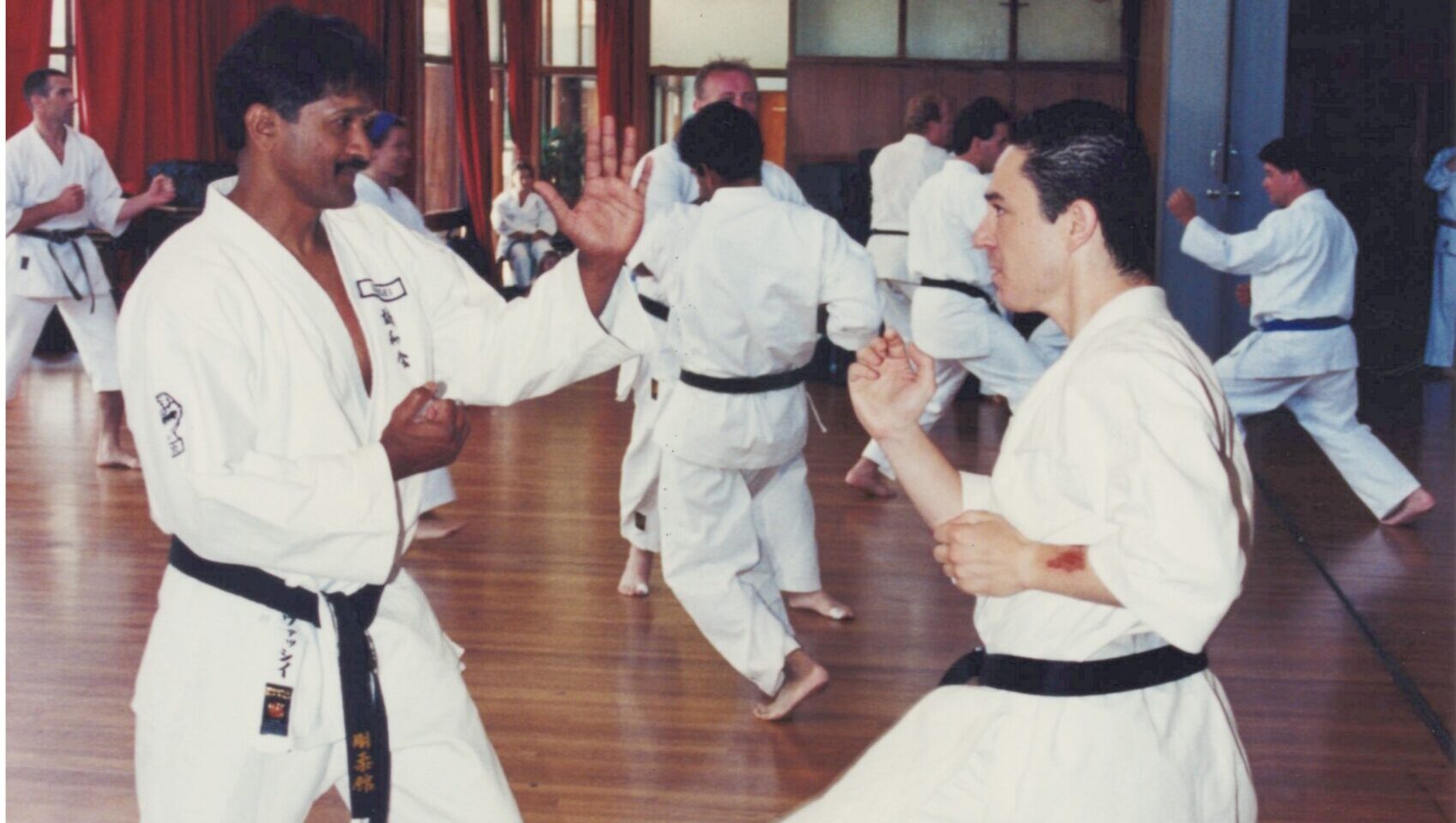 Historic 1995 photograph of a younger Vassie Shihan training on a wooden floor at a Goju-Ryu Seiwakai karate seminar in Japan, practicing dynamic hand drills with another black belt.