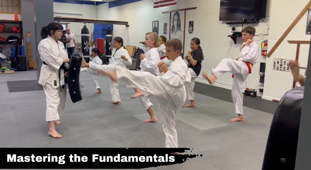 Young students in karate uniforms executing a controlled kick against a target pad to practice single-leg balance and coordination.