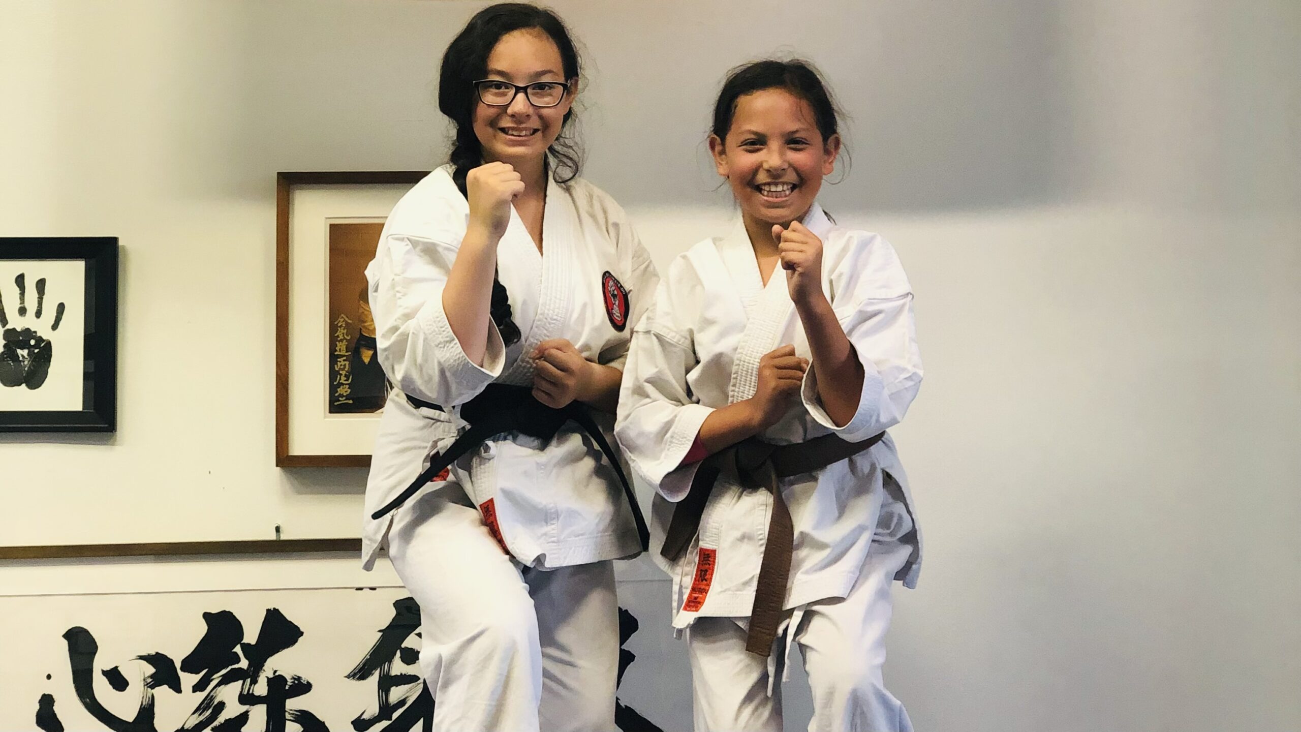 Two young karate students in white gis practicing focused front kicks on blue training mats at Karate of LA in West Los Angeles.