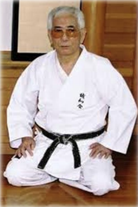 Seiwa-Kai Newsletter Issue 1 Cover Artwork - Photograph of Shuji Tasaki Hanshi in a White Gi and a Black Belt Kneeling on a Wooden Floor